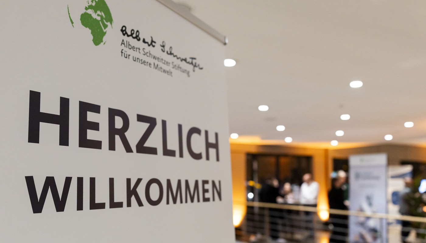 Roll-up 'Herzlich Willkommen' und Menschen im Hintergrund